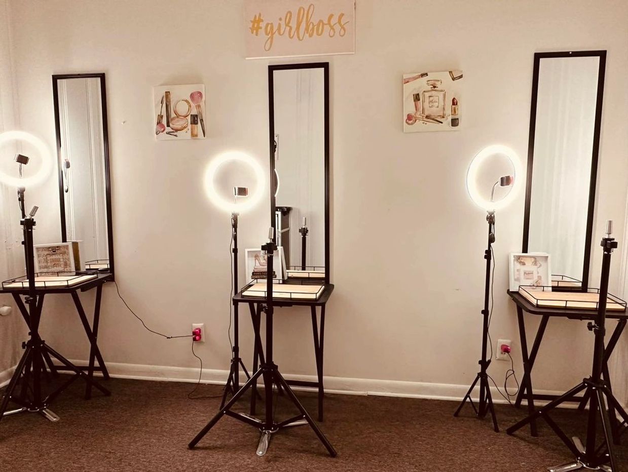 A makeup studio setup with mirrors, ring lights, and #girlboss sign.