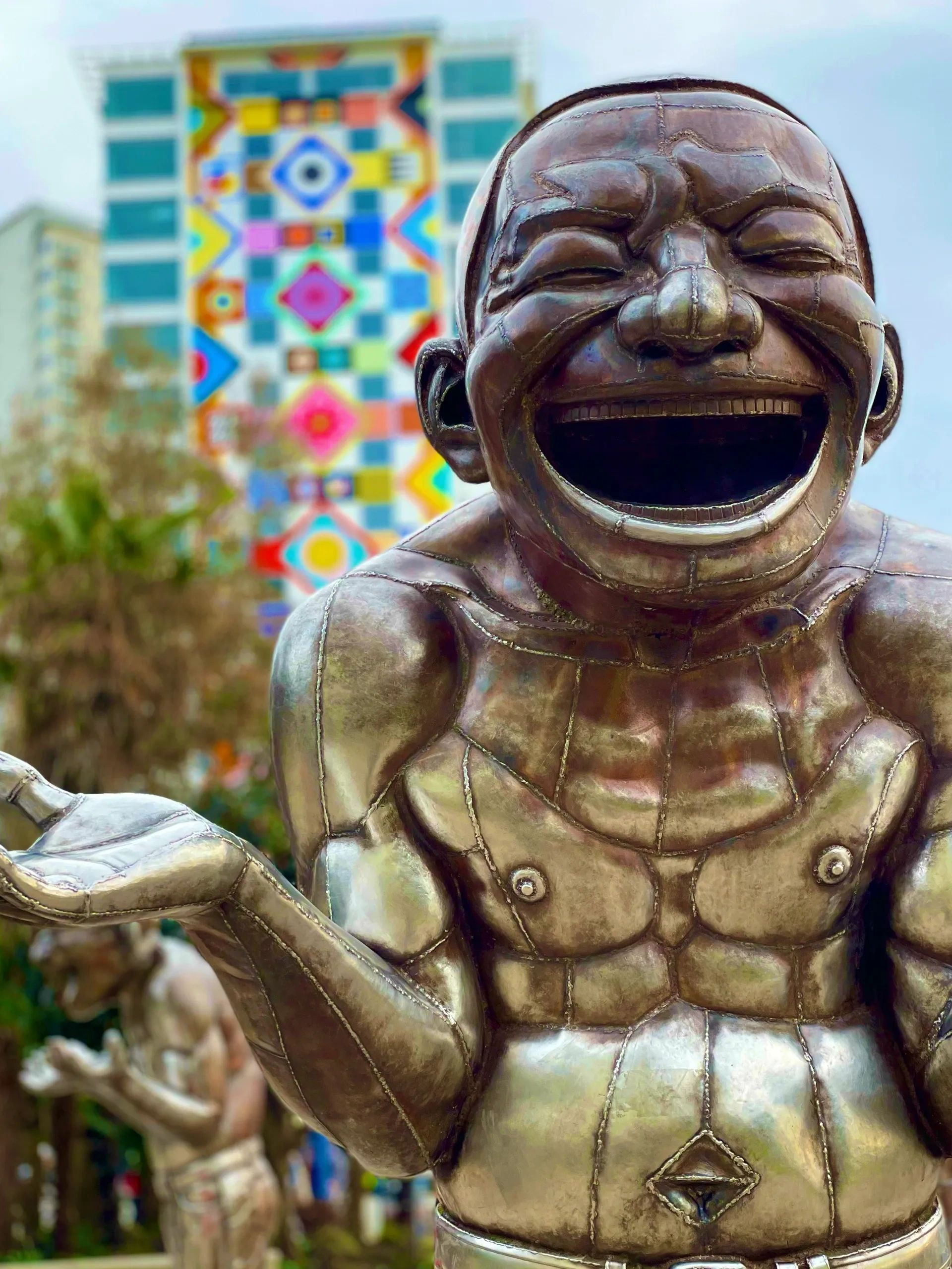 Bronze laughing statue with colorful geometric mural in background.