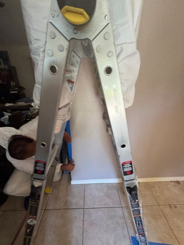 Person holding a metal ladder indoors on a tiled floor.