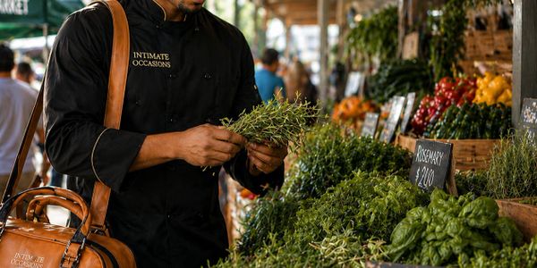 Man in black chef coat selecting fresh herbs at an outdoor market.