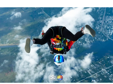 Skydiver performing a stunt above clouds with colorful gear and helmet.