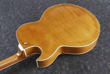 Back of a polished wooden guitar body on a dark surface.