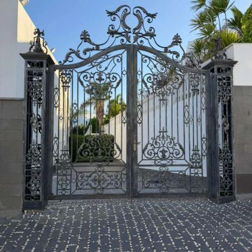 Elegant black wrought iron gate with intricate designs at a driveway.