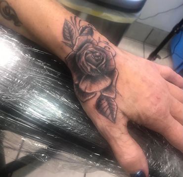 Black and gray rose tattoo on the back of a hand.