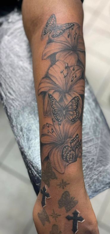 Black and grey tattoo of lilies and butterflies on forearm.