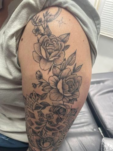 Black and grey floral tattoo with roses and leaves on upper arm.