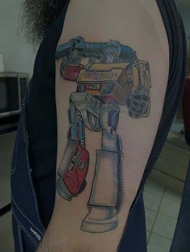 Colorful tattoo of a robot resembling a Transformer on a person's arm.