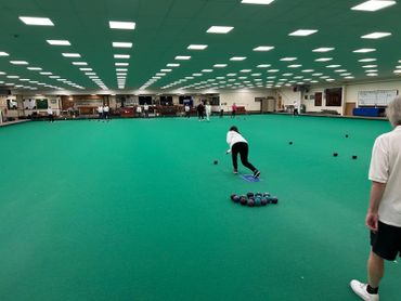 A woman bowling on an indoor bowls green