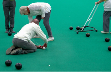 Two men measuring which bowls are nearest the jack. Another man collects bowls not in the count.