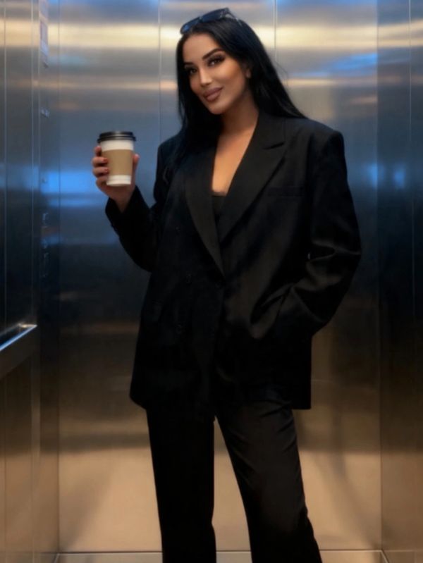 Woman in black suit holding coffee cup inside an elevator.