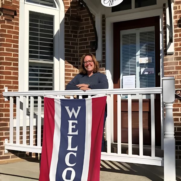 Woman smiling on porch with welcome flag