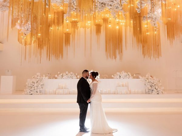 under a ceiling full of flowers and lights with hanging gold chain matching with light up bridal tabe