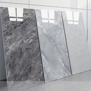 Three polished marble slabs with different gray patterns leaning against a wall.