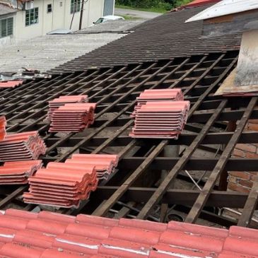 Roof tiles stacked on wooden roof framework under cloudy sky.