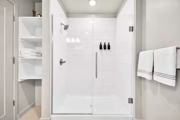 Modern white-tiled shower with glass doors and neatly arranged towels.