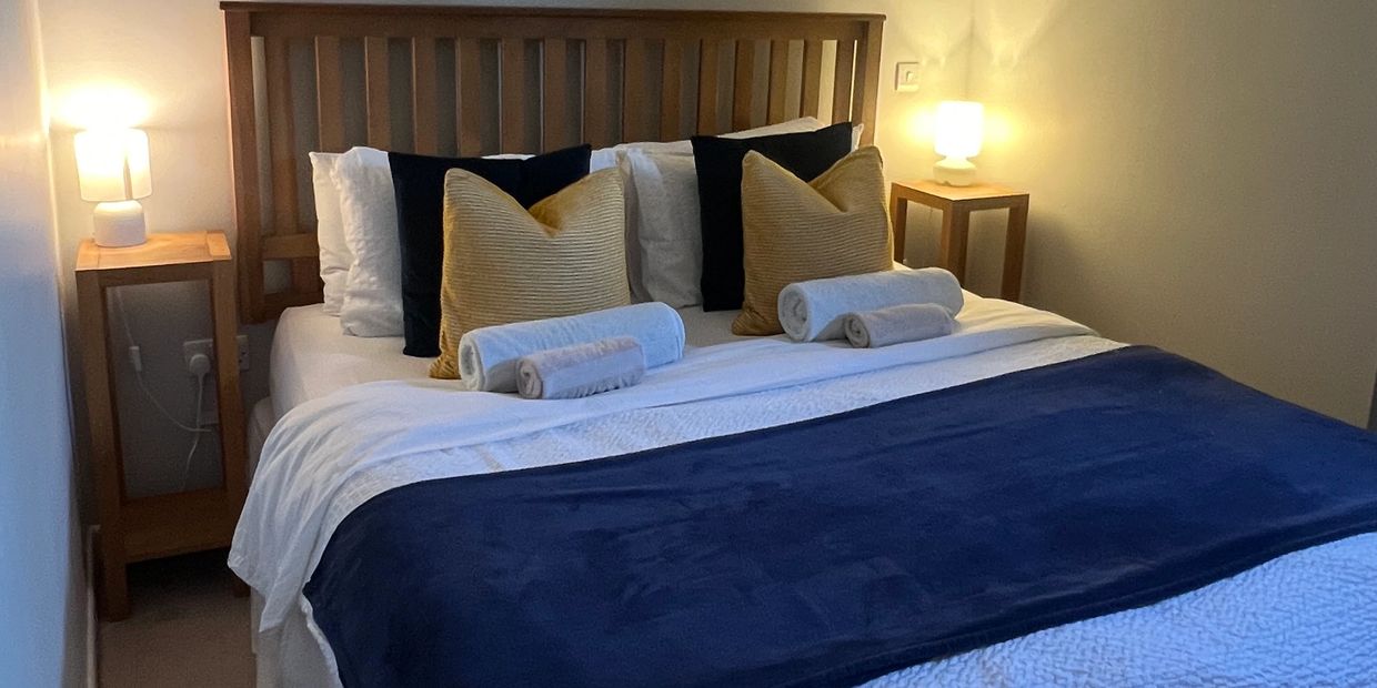 Neatly made bed with pillows, rolled towels, and bedside lamps.