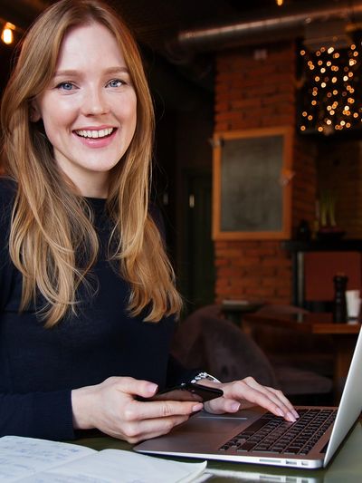 Woman smiling while using laptop and mobile phone
