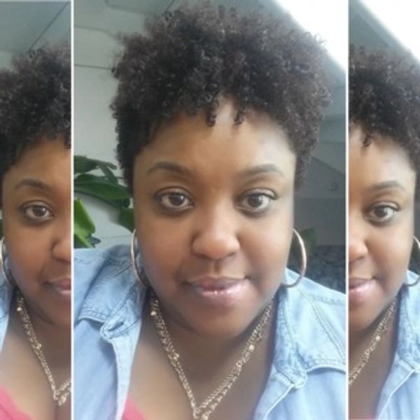 Woman with curly hair wearing hoop earrings and a denim jacket.
