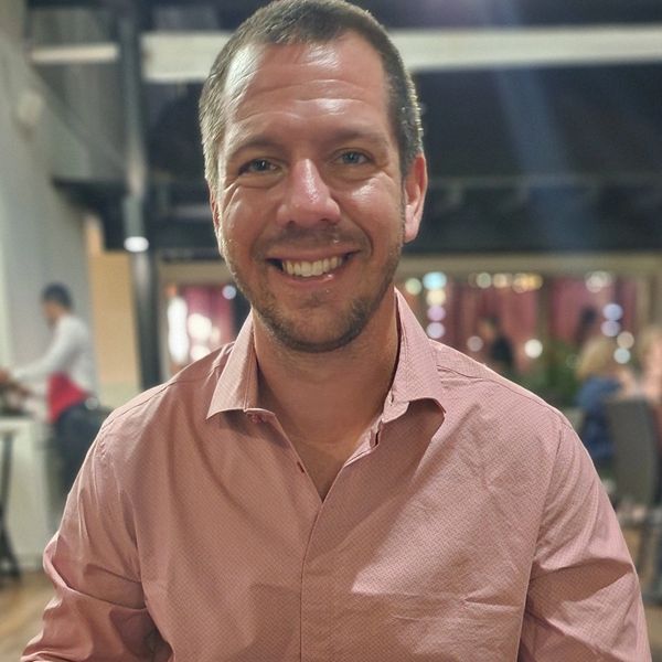 A headshot of a man with short brown hair and salmon colored shirt.