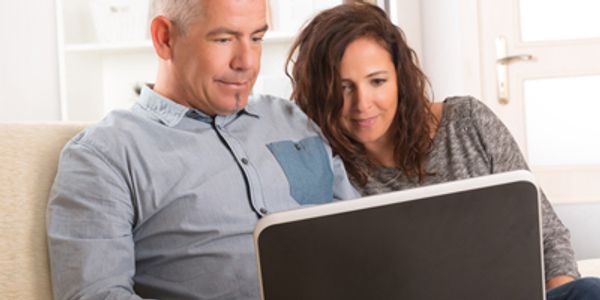 man and woman on a couch looking at a computer receiving online couples coaching