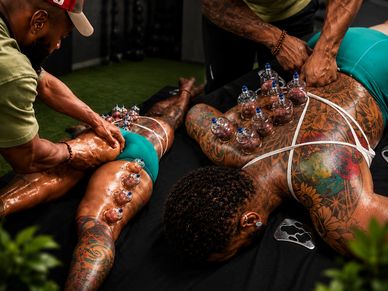 Two tattooed individuals receiving cupping therapy and massage on their backs.