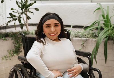 A smiling young woman in a wheelchair wearing a white long-sleeved top.