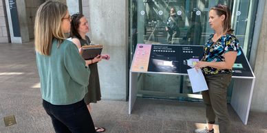 Three women in an airy-looking lobby talk together.