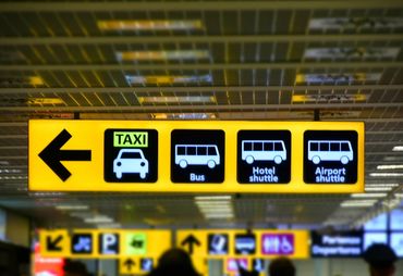 A bright yellow sign with black and white icons that read taxi, bus, hotel shuttle, airport shuttle.