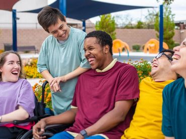 A group of five young people with disabilities wearing different colour t-shirts laugh together.