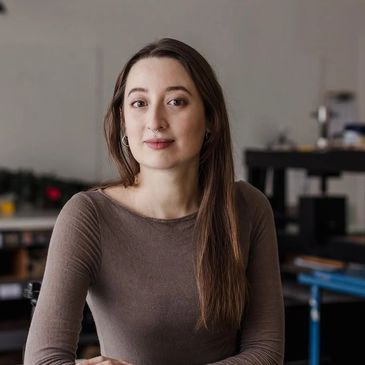 A white woman with long brown hair and red lipstick wears a brown shirt.