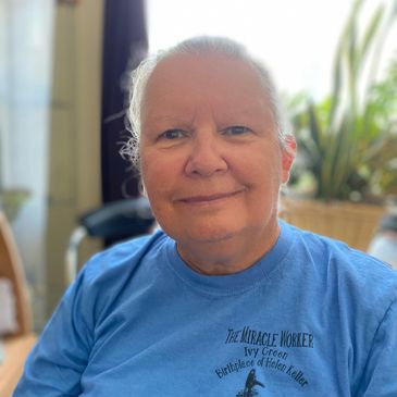 A smiling woman with white hair and a blue t-shirt.