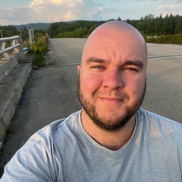 A bald man with short brown beard is wearing a grey tshirt and smiles into the camera.