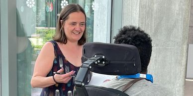 A smiling woman chats with a power wheelchair user.
