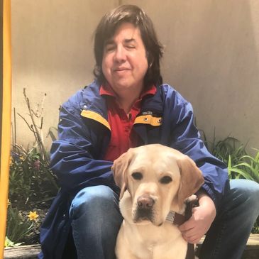 A man with brown hair wears a dark blue jacket and red top. He is sitting with a dog.