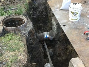 Open trench with a pipe repair near a manhole.