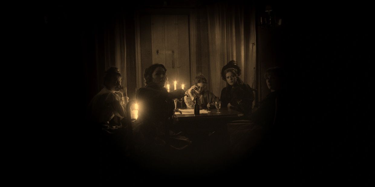 Five women gathered around a candlelit table in a dimly lit room.
