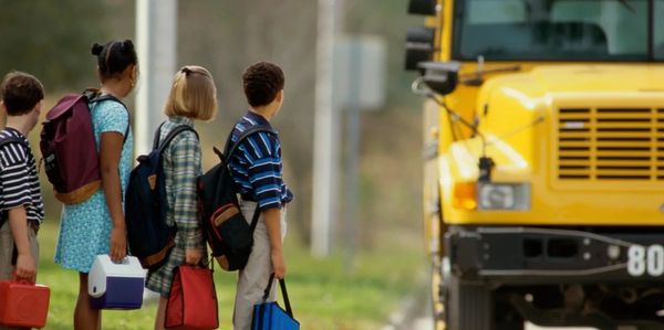 Children waiting to board a yellow school bus.