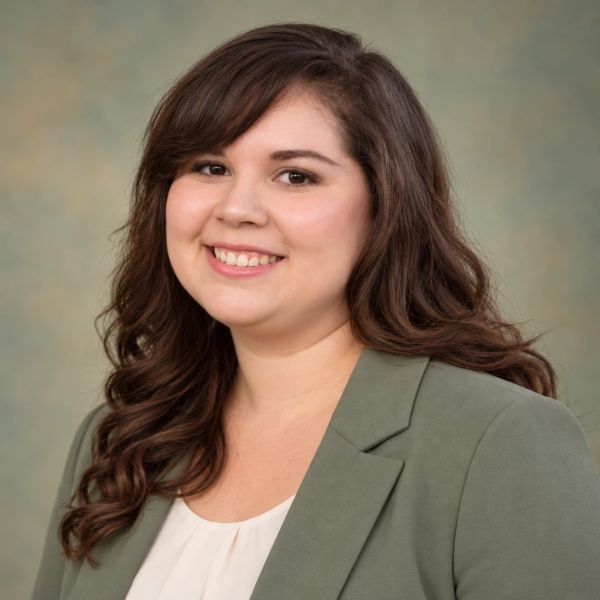 Smiling woman with wavy brown hair in a green blazer.
