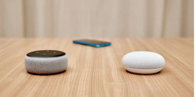 Two smart speakers and a smartphone on a wooden table.