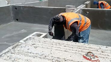 Workers in orange vests plastering concrete walls at a construction site.