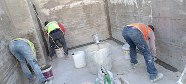 Three workers wearing safety vests plastering concrete walls inside a room.