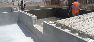 Two construction workers in orange vests working on a concrete structure under the sun.