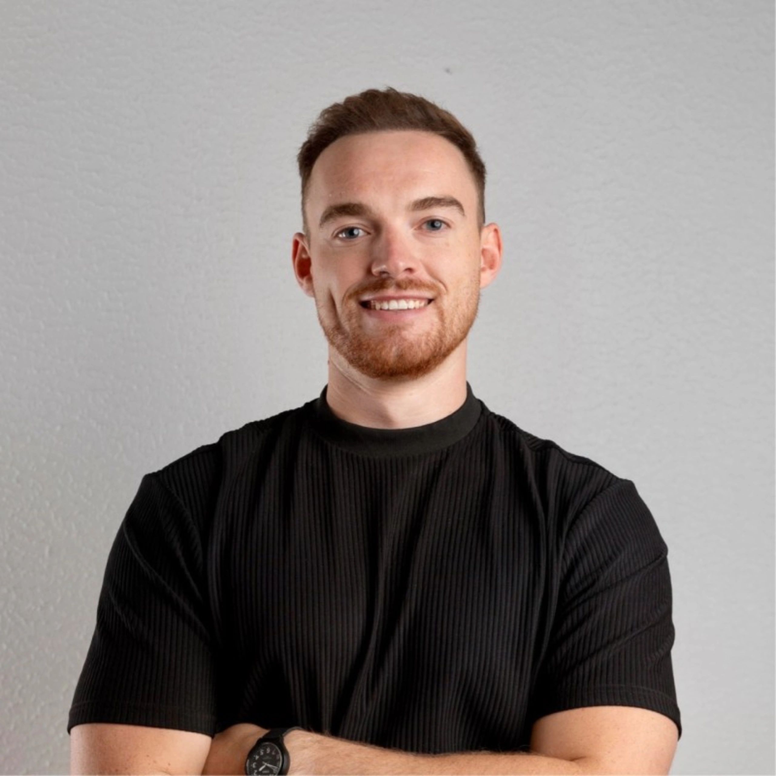 Smiling man in a black shirt with arms crossed against a plain background.