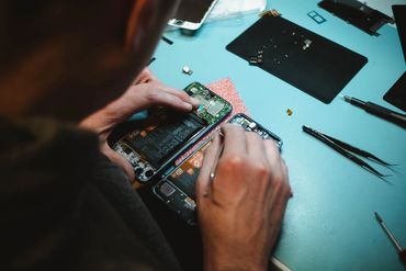 Person repairing two disassembled smartphones on a blue work table with tools.