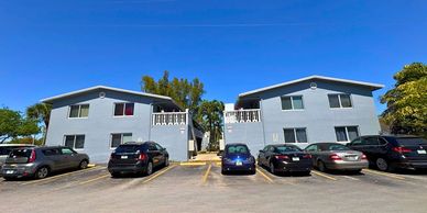 Two identical residential buildings with parked cars under a clear blue sky.