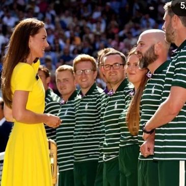 A woman in a yellow dress meets a group in green-striped uniforms at an outdoor event.