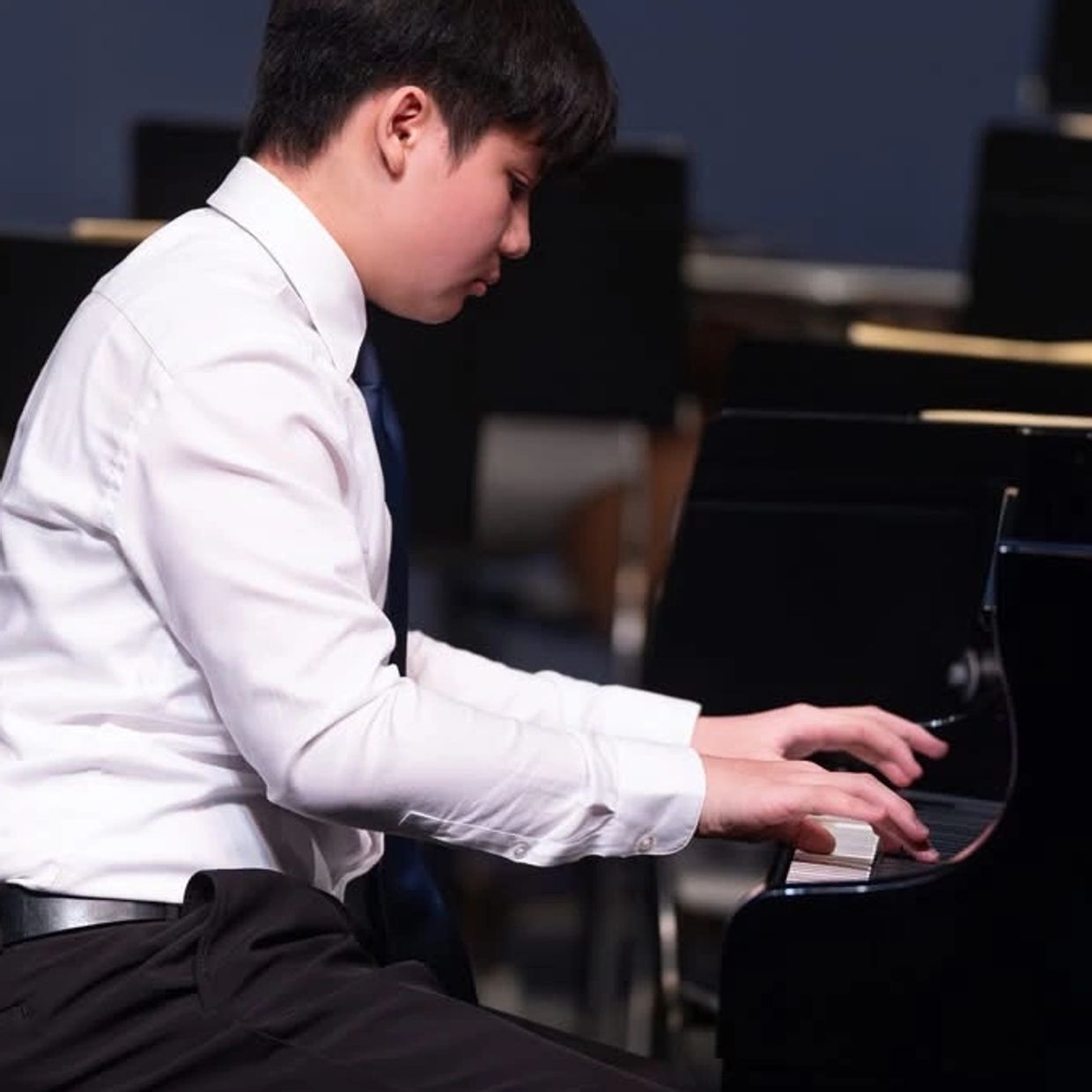 A young man in formal attire playing a piano with focus.