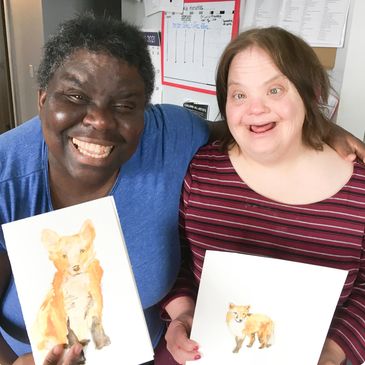 Two joyful women proudly showing their fox paintings.