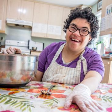 Happy person with gloves and apron cooking in a bright kitchen.