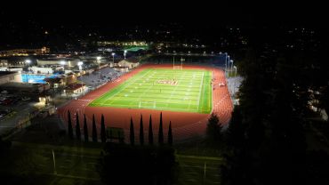 Night view of a well-lit sports field with a running track and a nearby swimming pool.